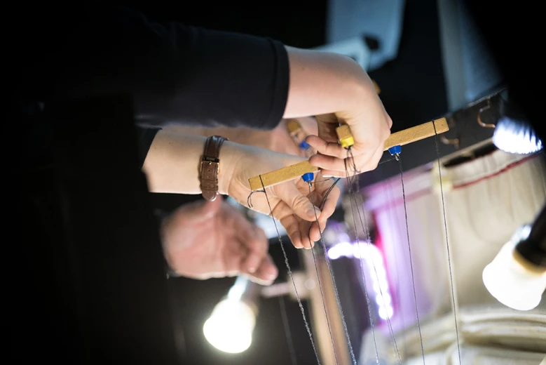 Hands operating the controls and strings of a marionette puppet.